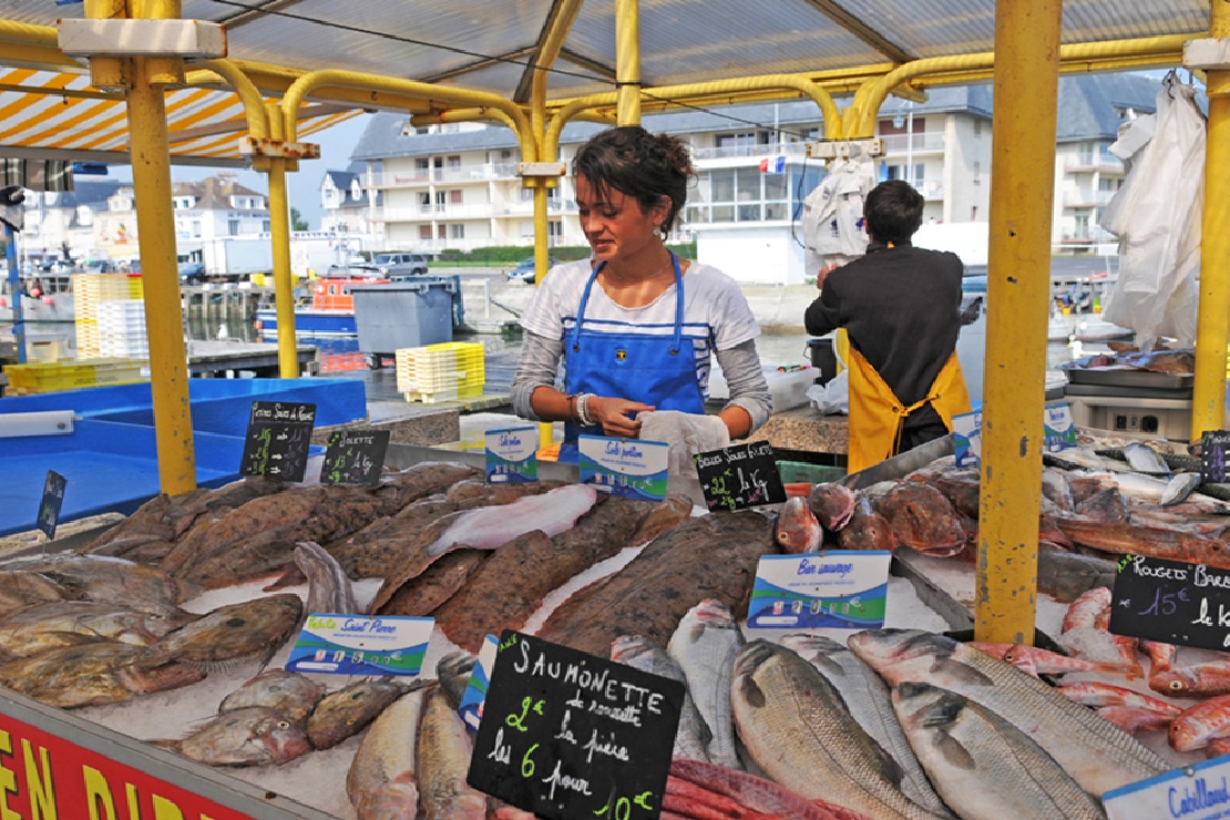 Vendeuse du port de Courseulles-sur-Mer derrière son étal rempli de poissons